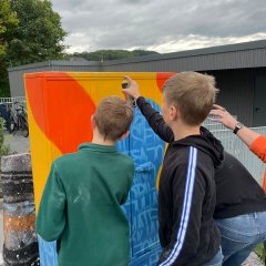 Des adolescents décorent la façade du boîtier électrique avec des dessins colorés.