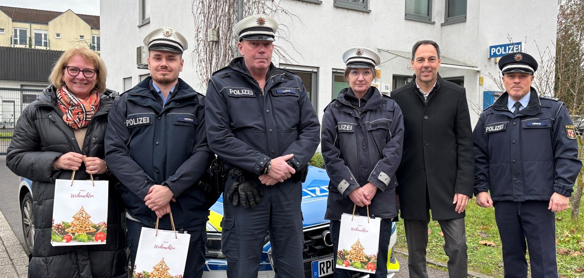 Burgemeester Wacht met medewerkers van het politiebureau in Konz voor het bureau en een politieauto tijdens de overhandiging van de cadeautassen.